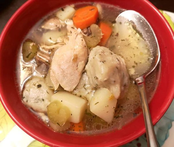 A bowl of traditional Acadian Fricot with chicken, fluffy dumplings, and vegetables in a savory broth