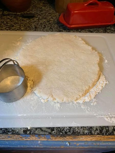 Biscuit dough rolled out on a floured surface, ready to be cut.