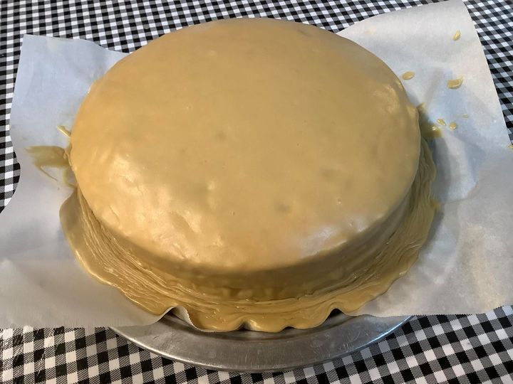 A classic caramel cake recipe with smooth, golden caramel icing, sitting on parchment paper and a checkered tablecloth