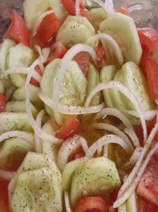 A large blue serving bowl overflowing with vibrant tri-color rotini pasta, chunky tomatoes, crisp cucumbers, black olives, cubed ham, and Colby Jack cheese, all tossed in a glossy Italian dressing.