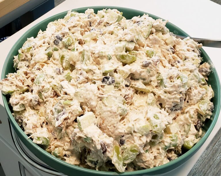 A large green bowl filled with a creamy Waldorf chicken salad featuring chopped apples, grapes, raisins, and walnuts.