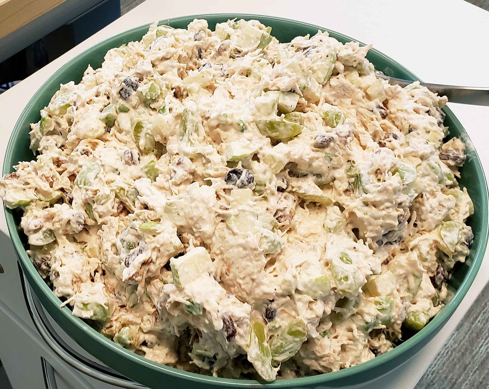 A large green bowl filled with a creamy Waldorf chicken salad featuring chopped apples, grapes, raisins, and walnuts.