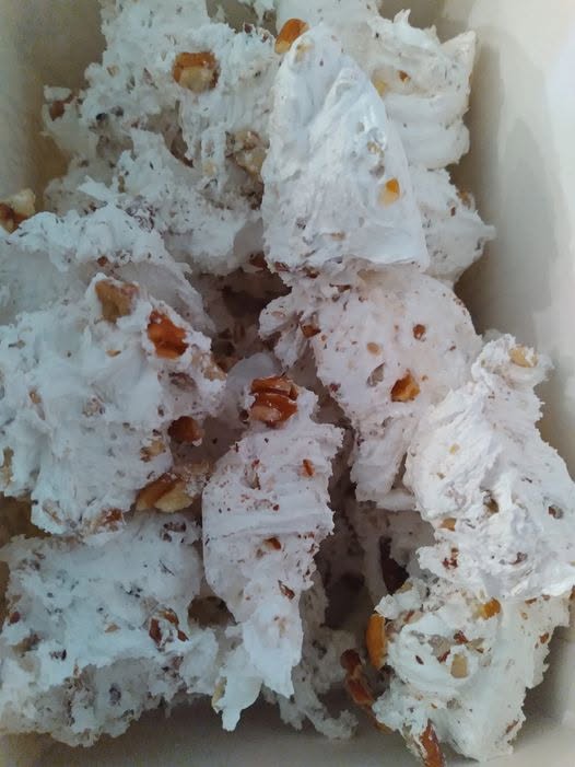 A pile of freshly made, fluffy white homemade divinity candy studded with chopped pecans inside a container.