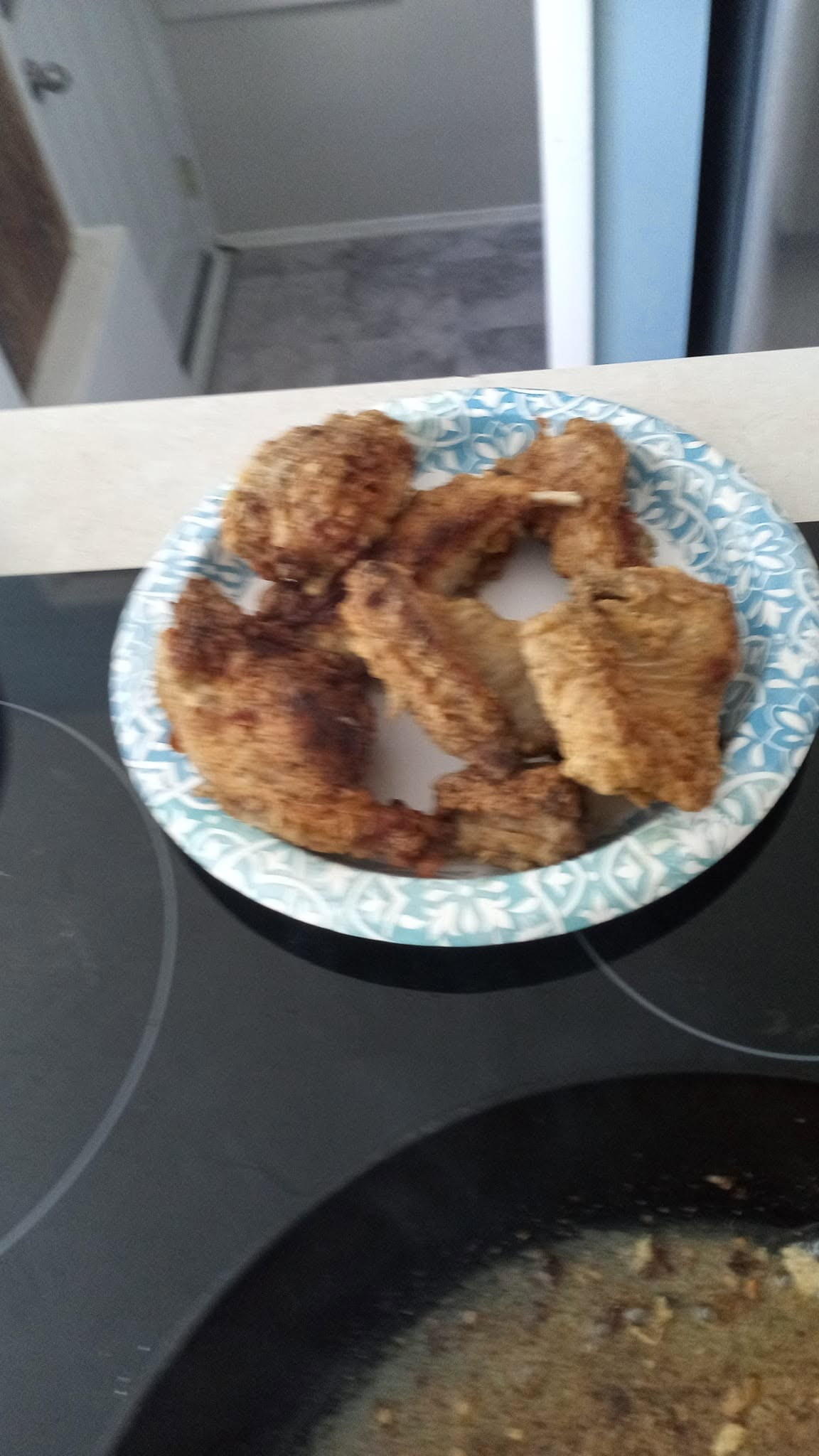 Freshly fried, golden-brown pieces of crispy fried rabbit resting on a blue patterned paper plate next to a cast-iron skillet.