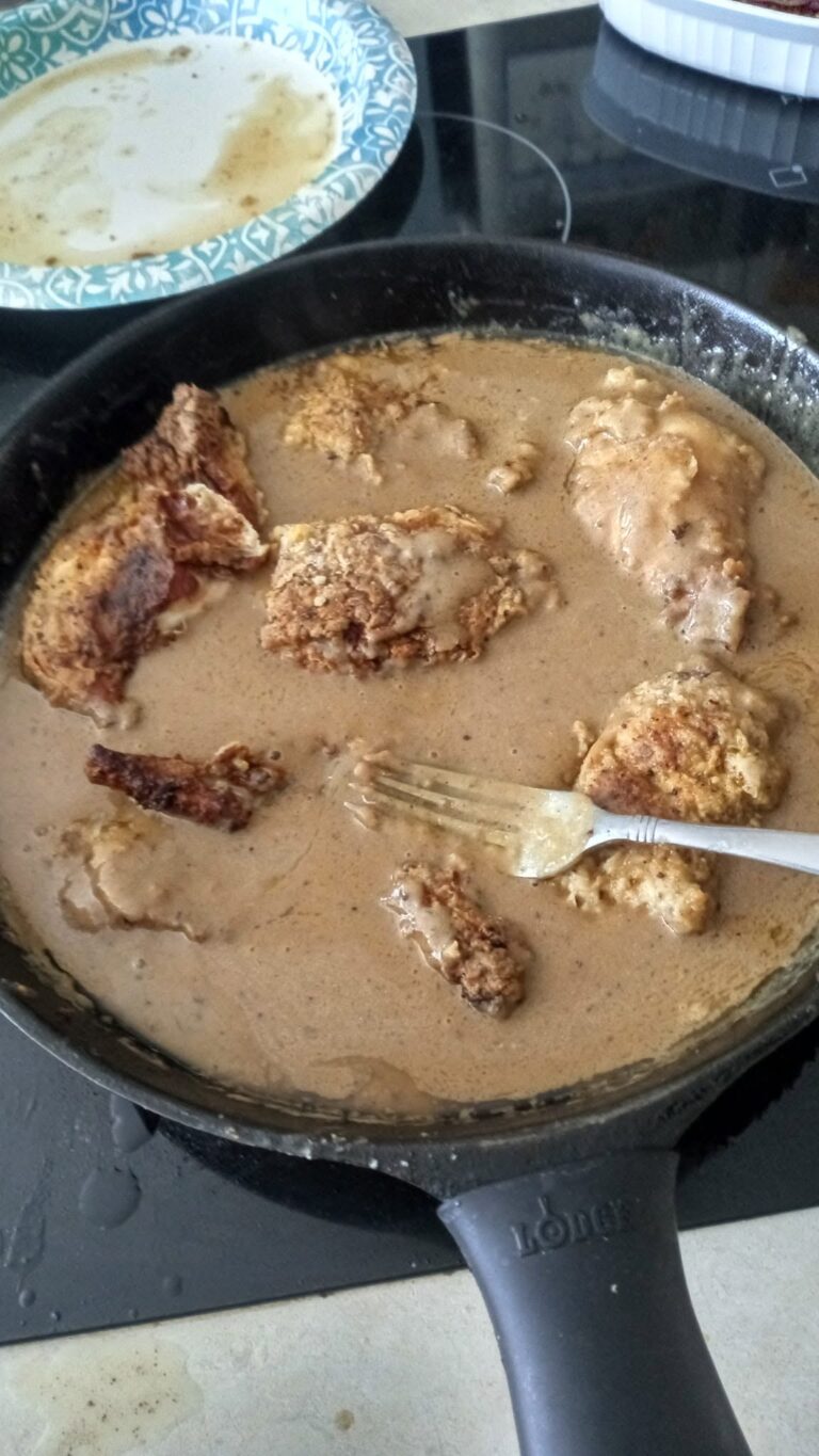 Battered rabbit pieces sizzling in a heavy black cast-iron skillet filled with hot oil and pan drippings.