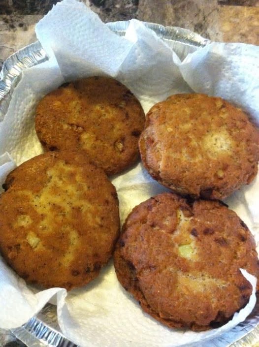 Four golden-brown, freshly fried salmon patties resting on paper towels in a foil-lined basket.