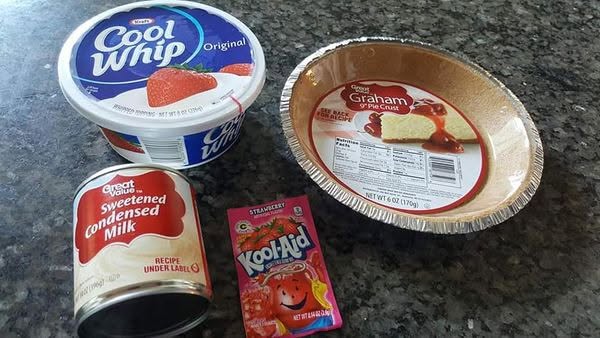 Ingredients for a Kool-Aid pie including a tub of Cool Whip, a can of sweetened condensed milk, a packet of strawberry Kool-Aid, and a store-bought graham cracker crust.