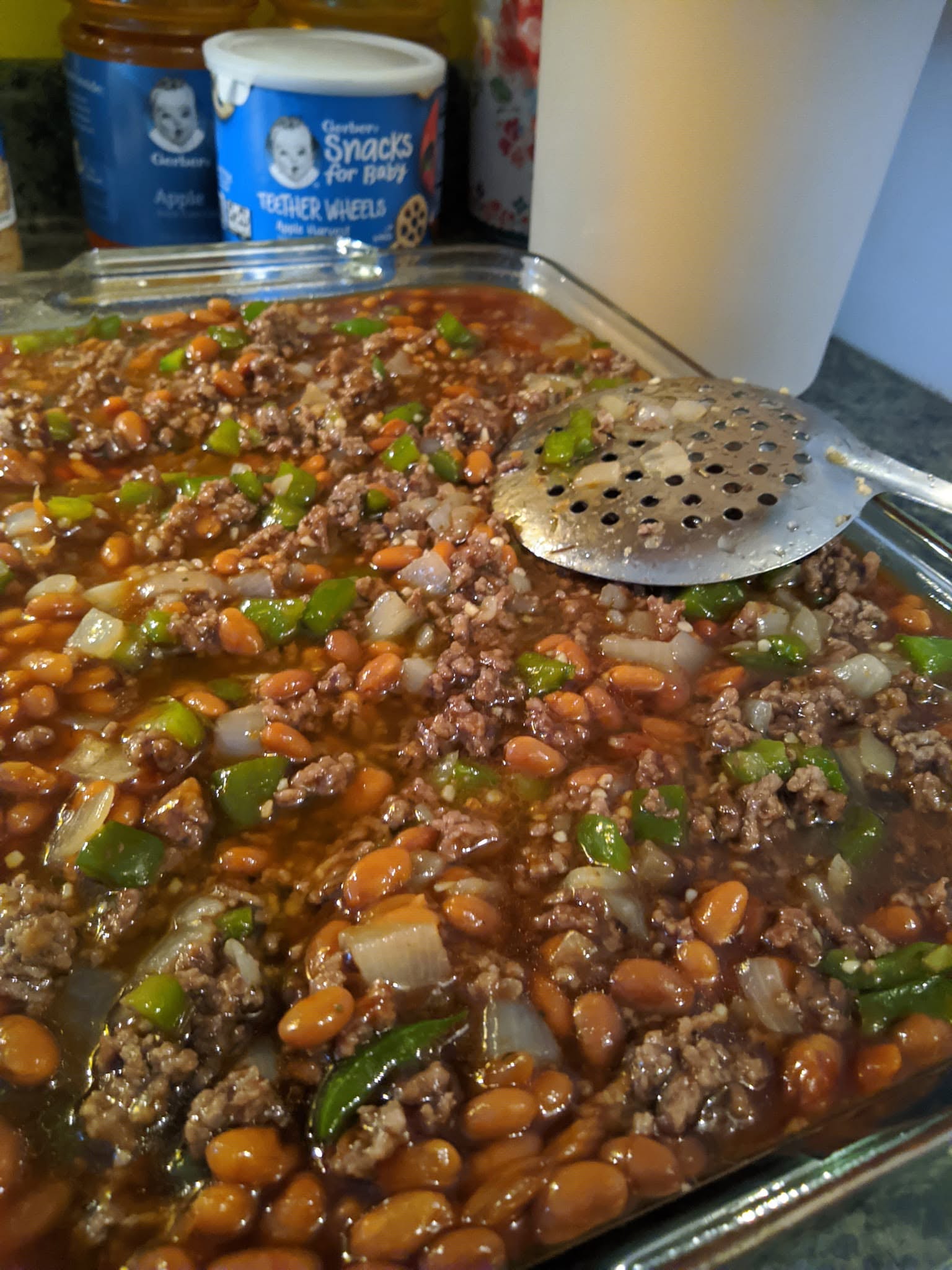 A large glass baking dish filled with a savory cowboy casserole featuring baked beans, ground beef, chopped onions, and green bell peppers.