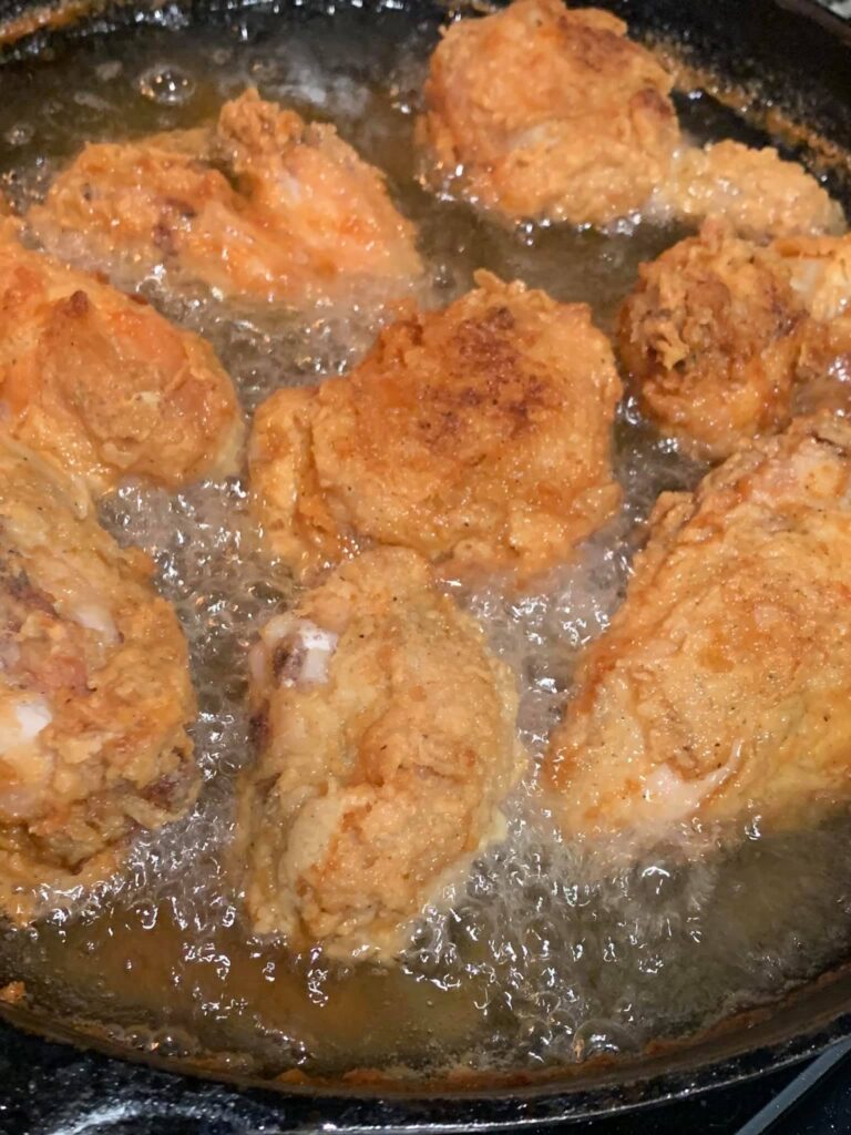 Golden brown, crispy fried chicken bubbling away in melted shortening inside a heavy cast-iron skillet.