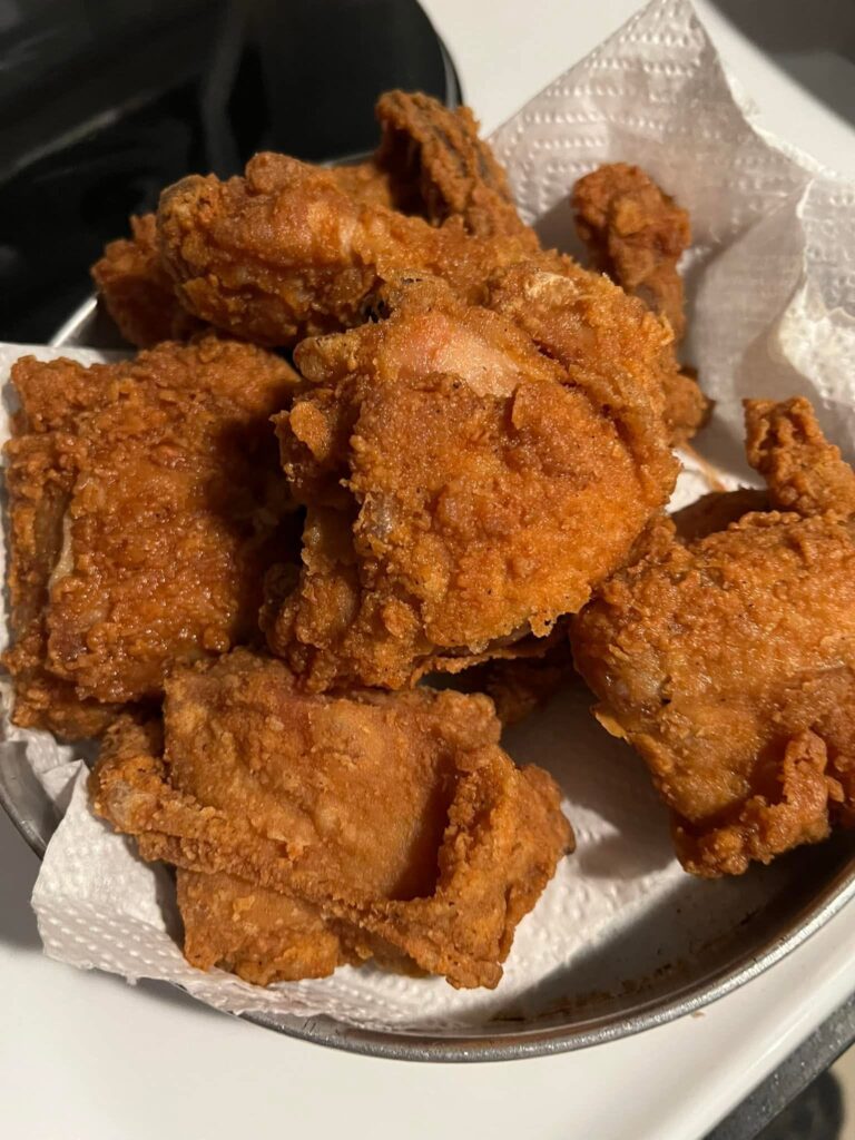 A pile of deeply golden, extra crispy fried chicken pieces resting on white paper towels inside a metal pan.