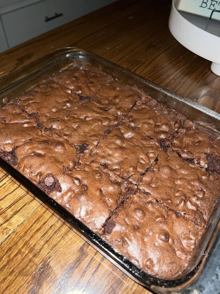 A glass baking pan filled with freshly baked, thick, and fudgy homemade chocolate chip brownies cut into squares.