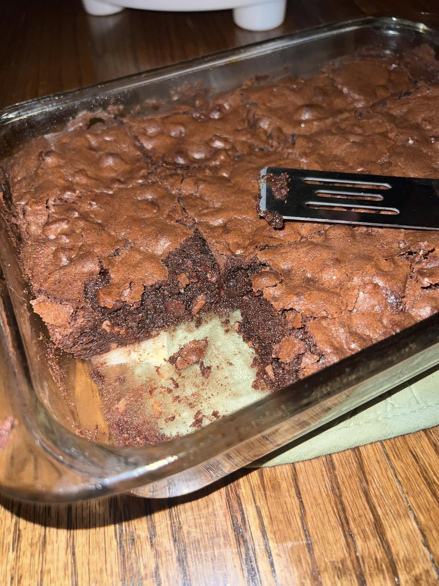 A close-up of a glass baking dish with a square of brownie removed with a spatula, showing the incredibly dense, gooey, and fudgy interior.