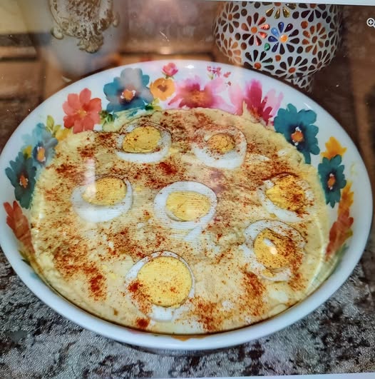 A large floral bowl filled with creamy, yellow mustard-based Southern tater salad, topped with meticulously arranged hard-boiled egg slices and a heavy dusting of paprika.