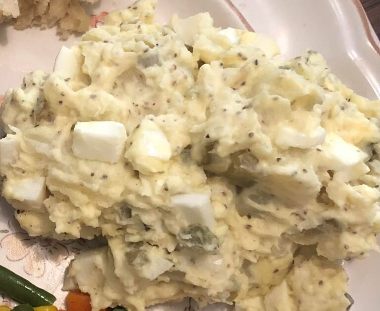 A large bowl of creamy, mustard-based Carolina style potato salad speckled with celery seeds and chunks of hard-boiled eggs.