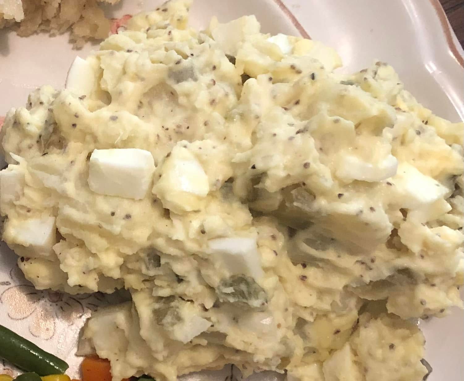 A large bowl of creamy, mustard-based Carolina style potato salad speckled with celery seeds and chunks of hard-boiled eggs.