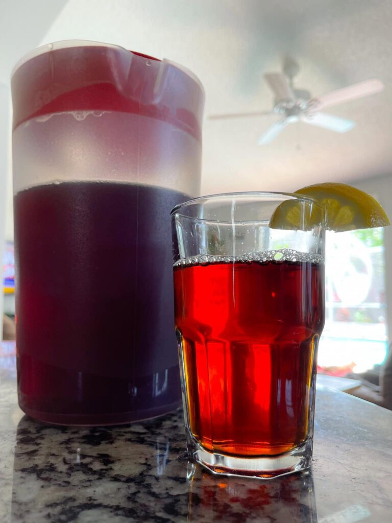 A tall glass and a large pitcher filled with a dark, rich, and strong brew of traditional Southern iced sweet tea, garnished with a fresh lemon slice.
