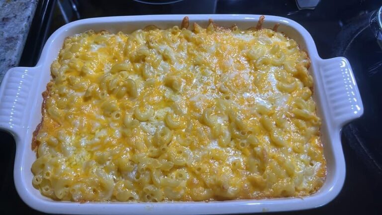 A white casserole dish filled with freshly baked macaroni and cheese, featuring a bubbly, golden-brown crust of melted cheddar and Colby Jack cheeses.