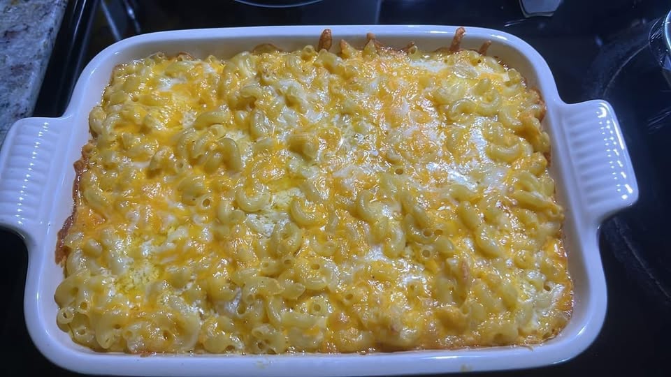 A white casserole dish filled with freshly baked macaroni and cheese, featuring a bubbly, golden-brown crust of melted cheddar and Colby Jack cheeses.