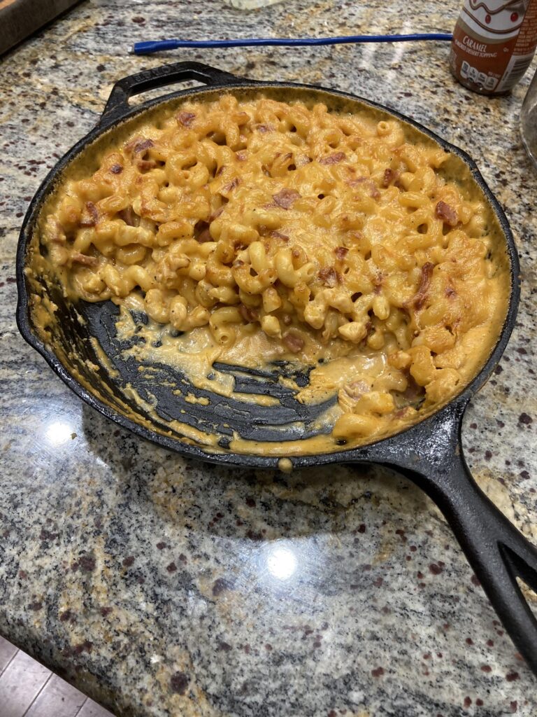 A large black cast iron skillet filled with ultra-creamy homemade baked macaroni and cheese, with a portion scooped out to show the gooey cheese sauce.