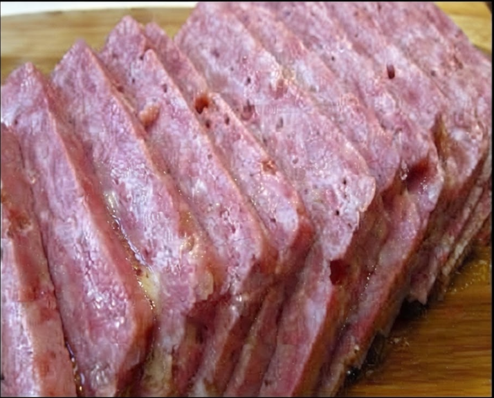 A wooden cutting board displaying a large block of homemade SPAM perfectly sliced into even, pink, rectangular pieces