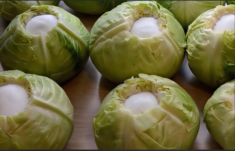 Several whole green cabbages with their cores hollowed out and filled with bright white salt, sitting on a wooden surface preparing for fermentation.