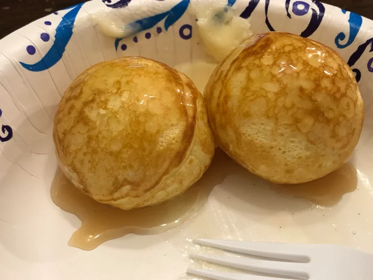 Two golden, perfectly round Danish Aebleskivers sitting on a plate and heavily drizzled with sweet breakfast syrup.
