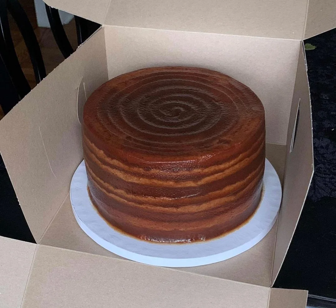 A whole, uncut 10-layer Appalachian Apple Stack Cake coated in smooth, dark spiced apple filling sitting in a cardboard bakery box.