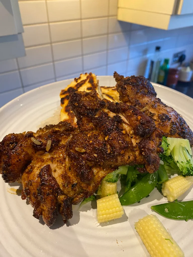 Three perfectly blackened, juicy chicken thighs served on a white plate alongside fresh green vegetables and baby corn.