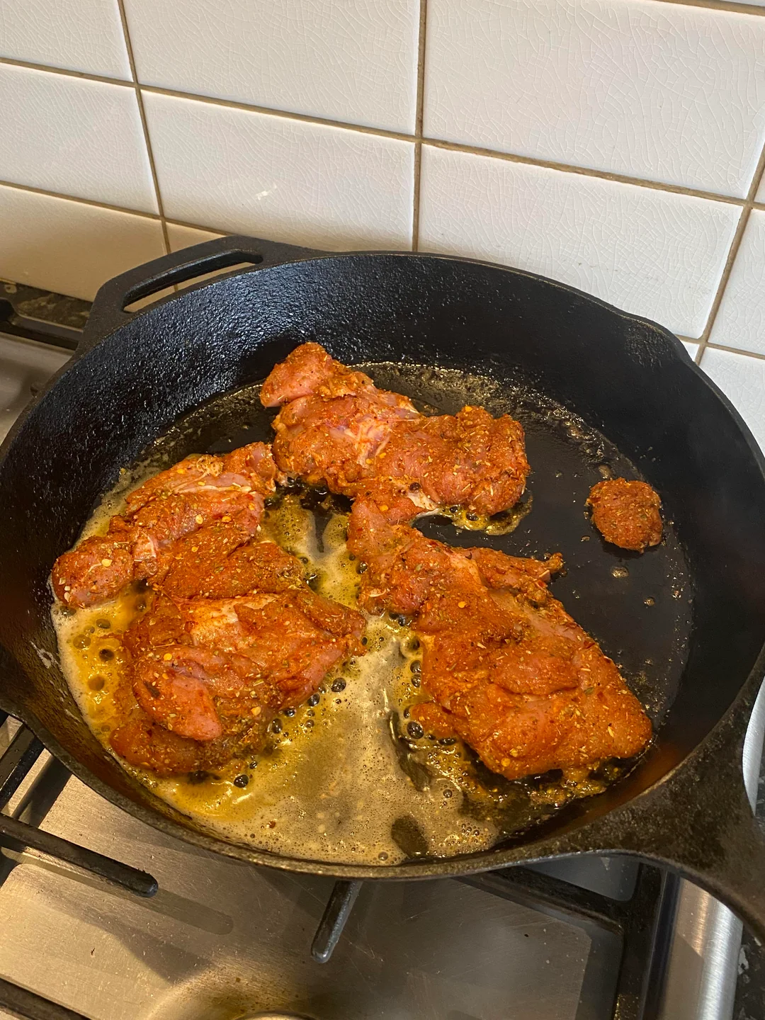 Seasoned chicken thighs searing in a pool of bubbling butter and oil inside a black cast iron skillet on a stovetop.