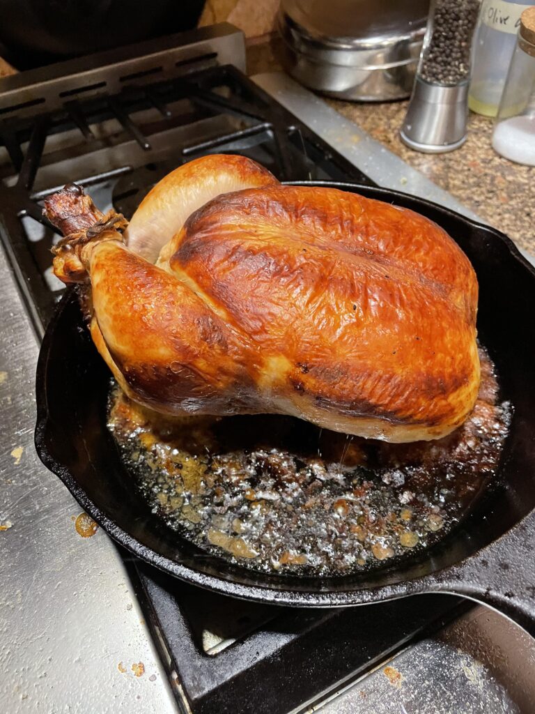 A whole buttermilk-marinated chicken, perfectly roasted to a deep golden brown, resting in a cast-iron skillet with savory pan drippings.