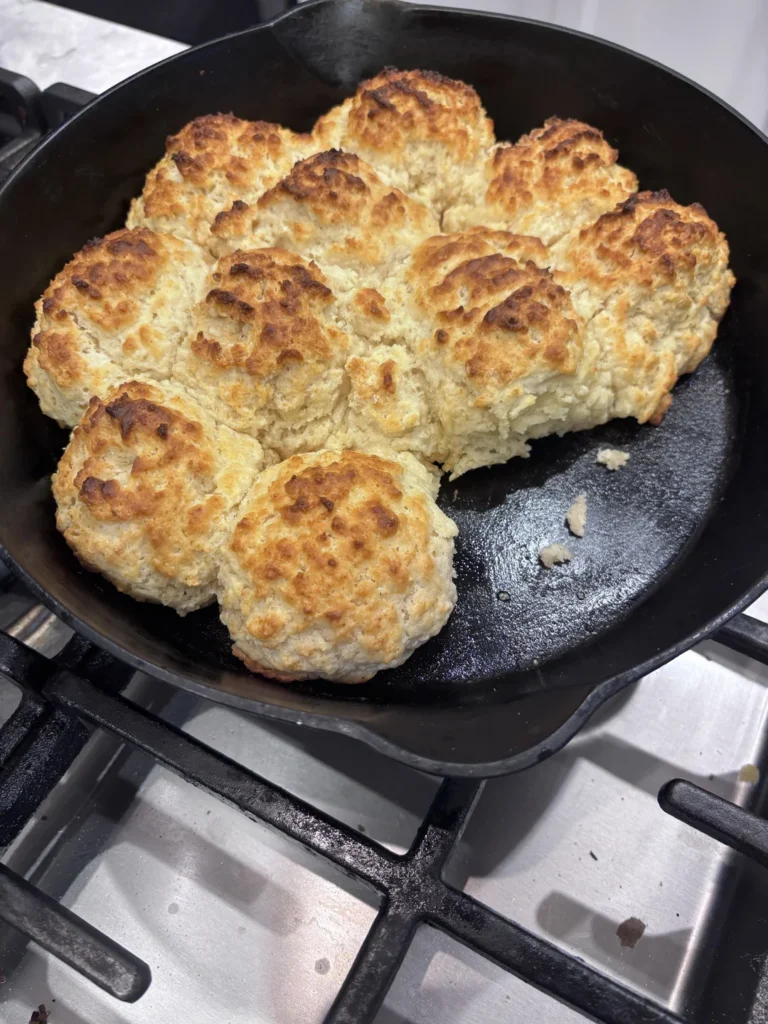 A cast iron skillet filled with large, golden-brown, freshly baked cat head biscuits with craggy, crispy crusts.