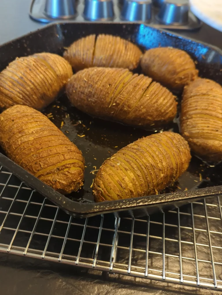Golden-brown, perfectly sliced Hasselback potatoes roasted with herbs in a dark cast iron skillet resting on a wire cooling rack.