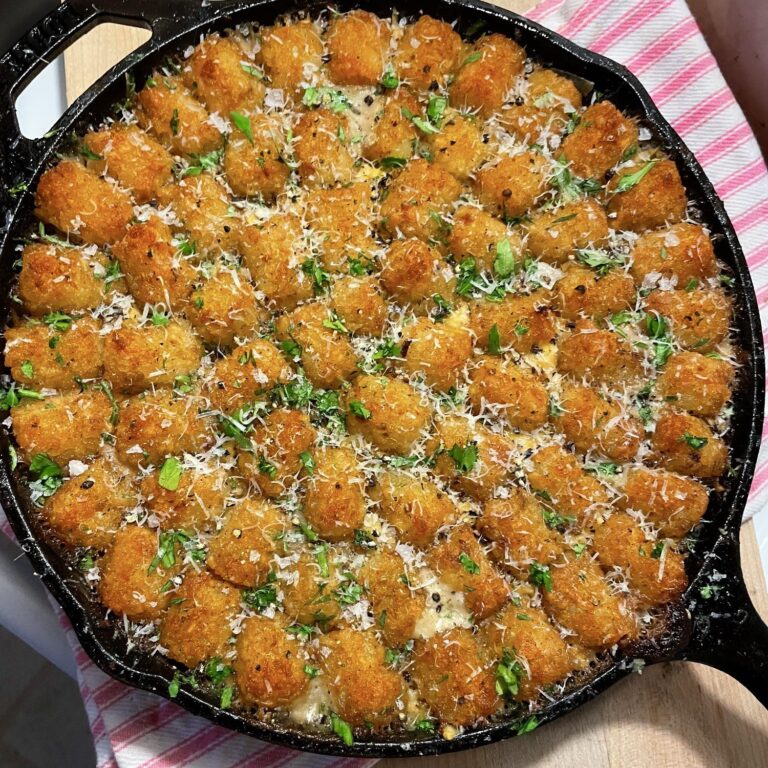 A large cast-iron skillet filled with a golden, perfectly tiled layer of crispy tater tots, garnished with grated parmesan, fresh parsley, and Maldon sea salt.