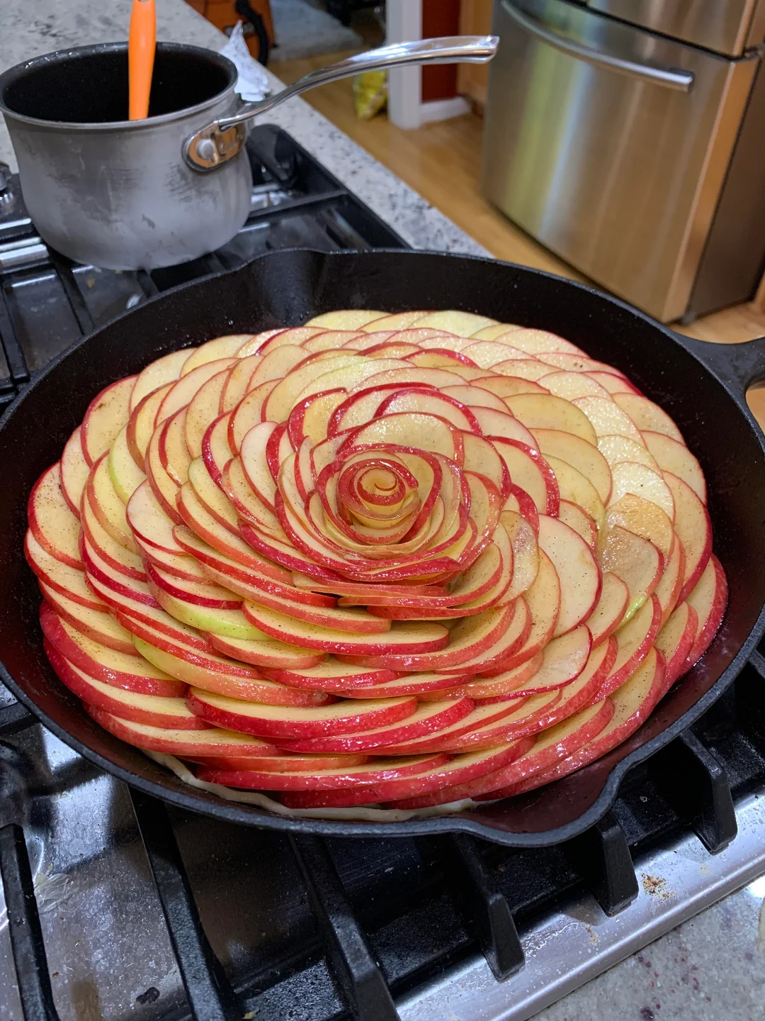 Thinly sliced red apples meticulously arranged in a stunning giant rose pattern inside a black cast-iron skillet before baking.