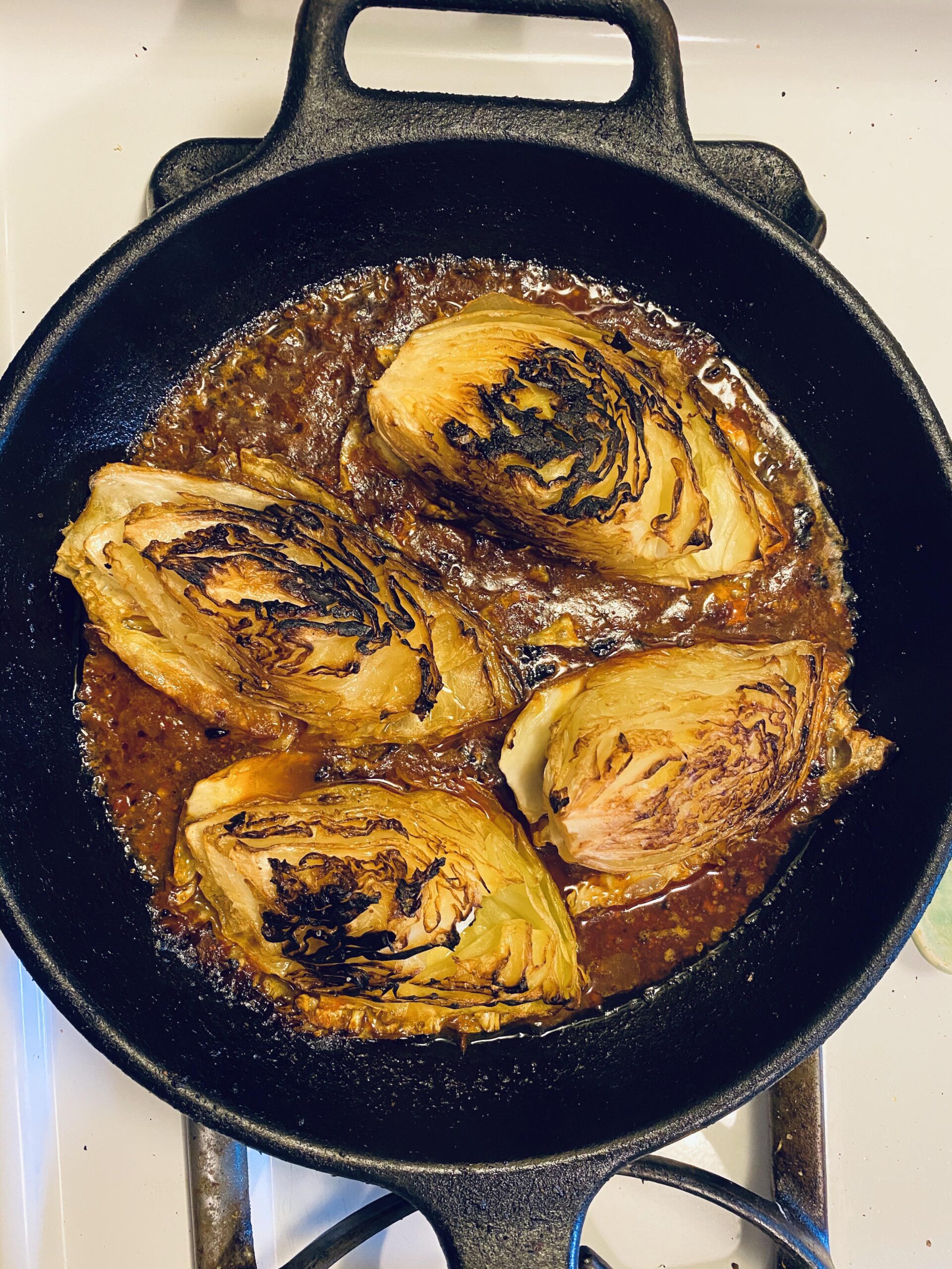 Four wedges of deeply charred, caramelized green cabbage simmering in a rich, savory brown broth inside a large cast iron skillet.