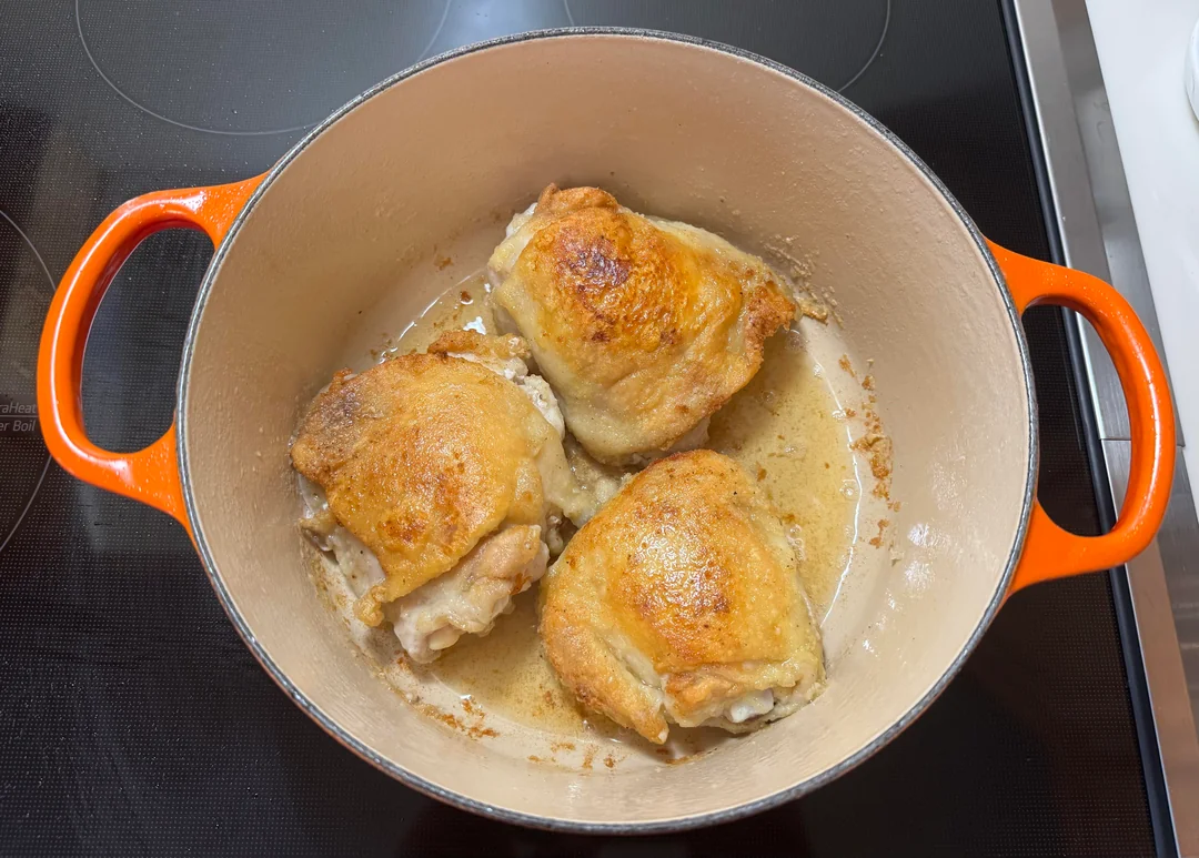 Three bone-in chicken thighs with crispy, golden skin searing in the bottom of an enameled Dutch oven.
