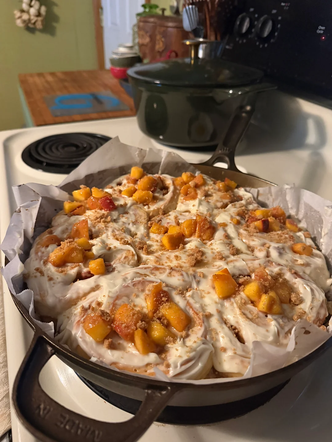 Freshly baked peach cobbler cinnamon rolls bubbling in their skillet, cooling slightly before frosting.