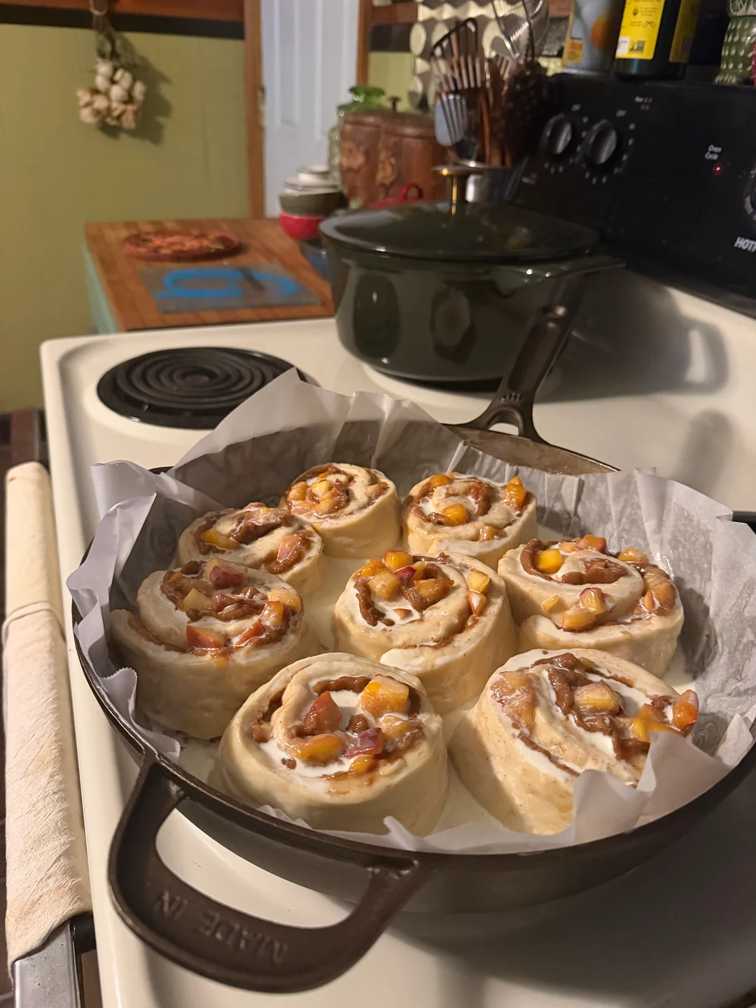 Risen cinnamon rolls in a cast iron skillet, drenched with heavy cream poured over and around them before baking.