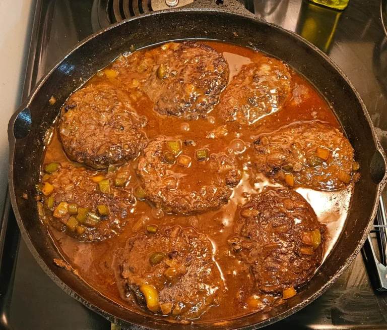 A hearty plate of smothered hamburgers covered in rich brown onion and pepper gravy, served over fluffy white rice with a side of mixed vegetables, with bottles of Crystal and Tabasco hot sauce in the background