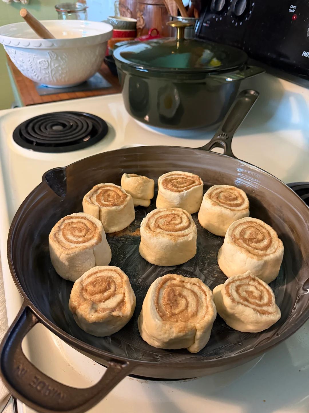 Sliced sourdough cinnamon rolls spaced out inside a greased 12-inch cast-iron skillet before their final rise.