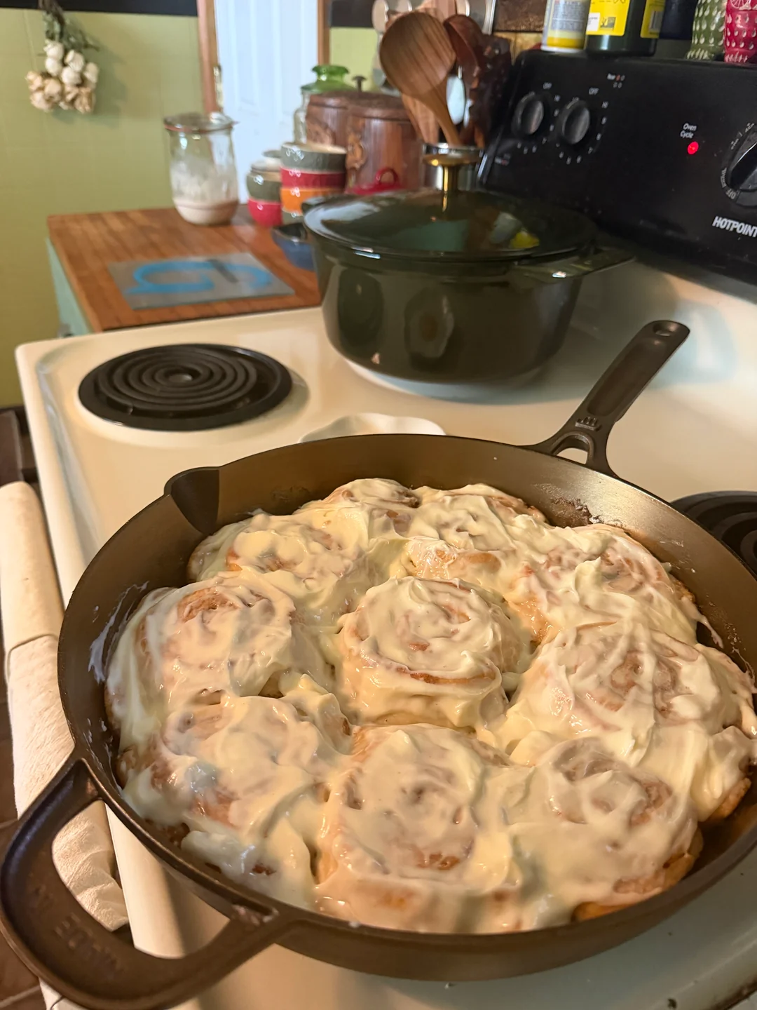 Freshly baked sourdough cinnamon rolls smothered in a thick layer of homemade cream cheese frosting inside a cast-iron skillet.