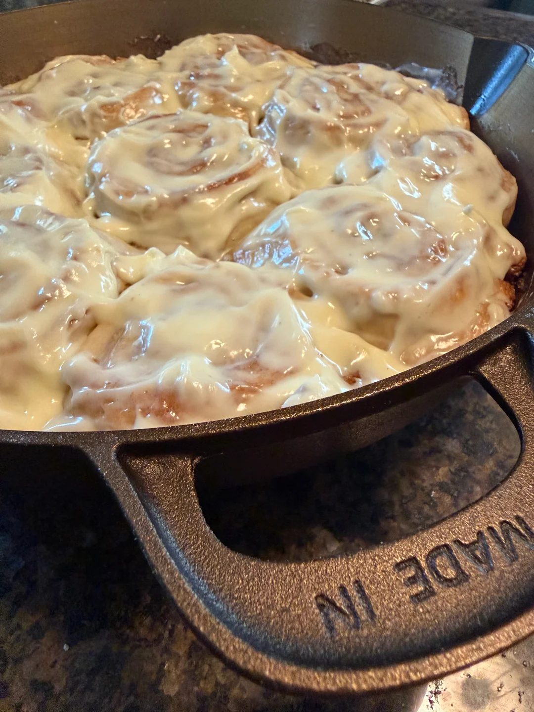 A finished batch of frosted sourdough cinnamon rolls resting on a stovetop, ready to be served.