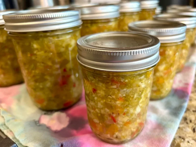 Rows of sealed glass mason jars filled with homemade green and red vegetable Chow Chow relish resting on a colorful towel.