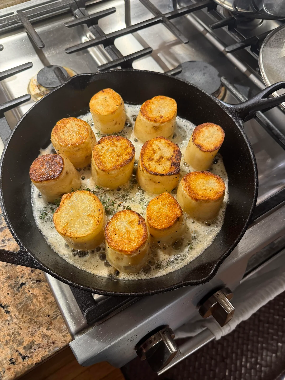 Six perfectly roasted fondant potatoes arranged on a white plate, garnished with fresh thyme sprigs.