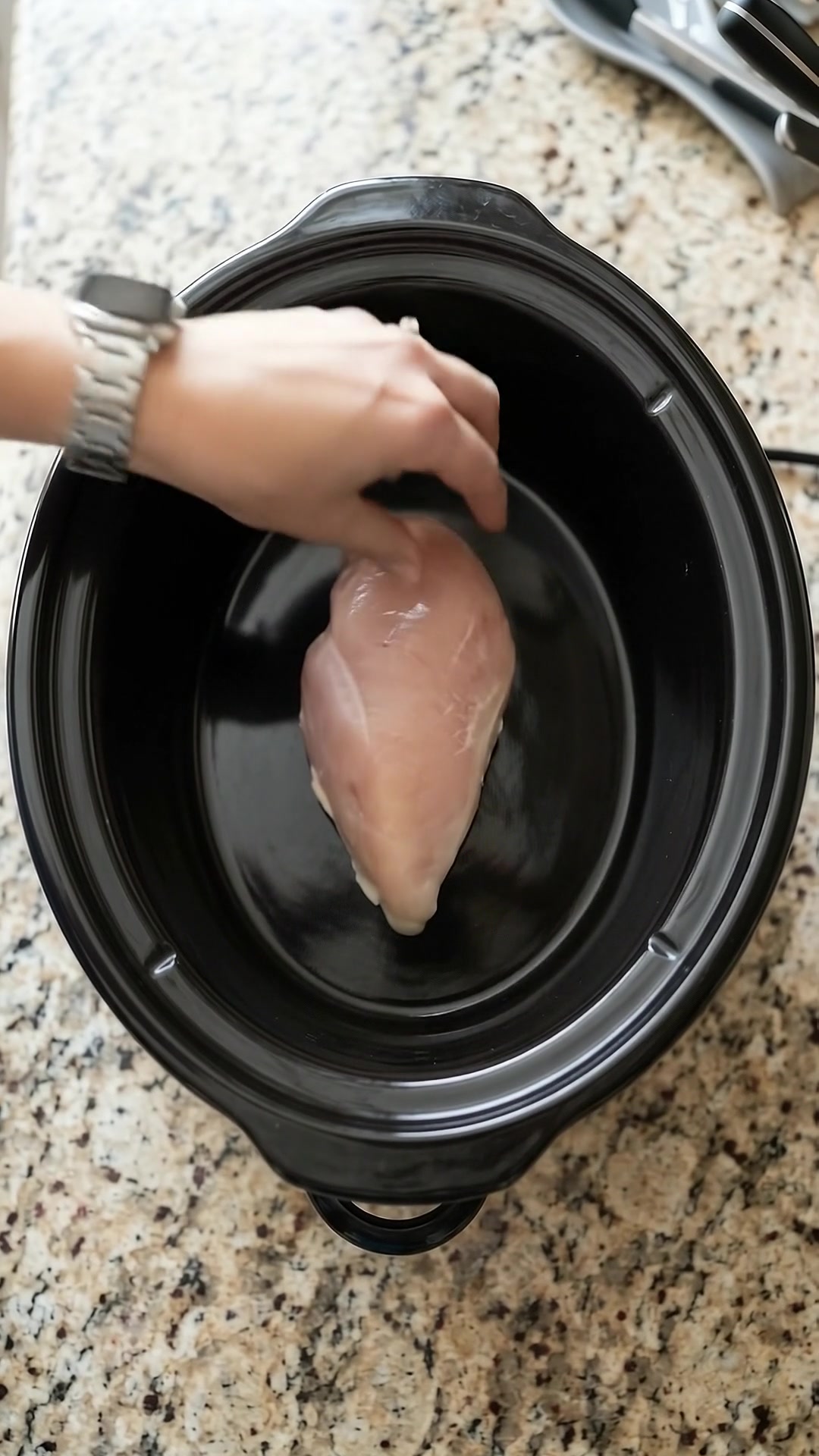 Raw boneless chicken breast being placed inside a slow cooker for cheesy chicken and broccoli.