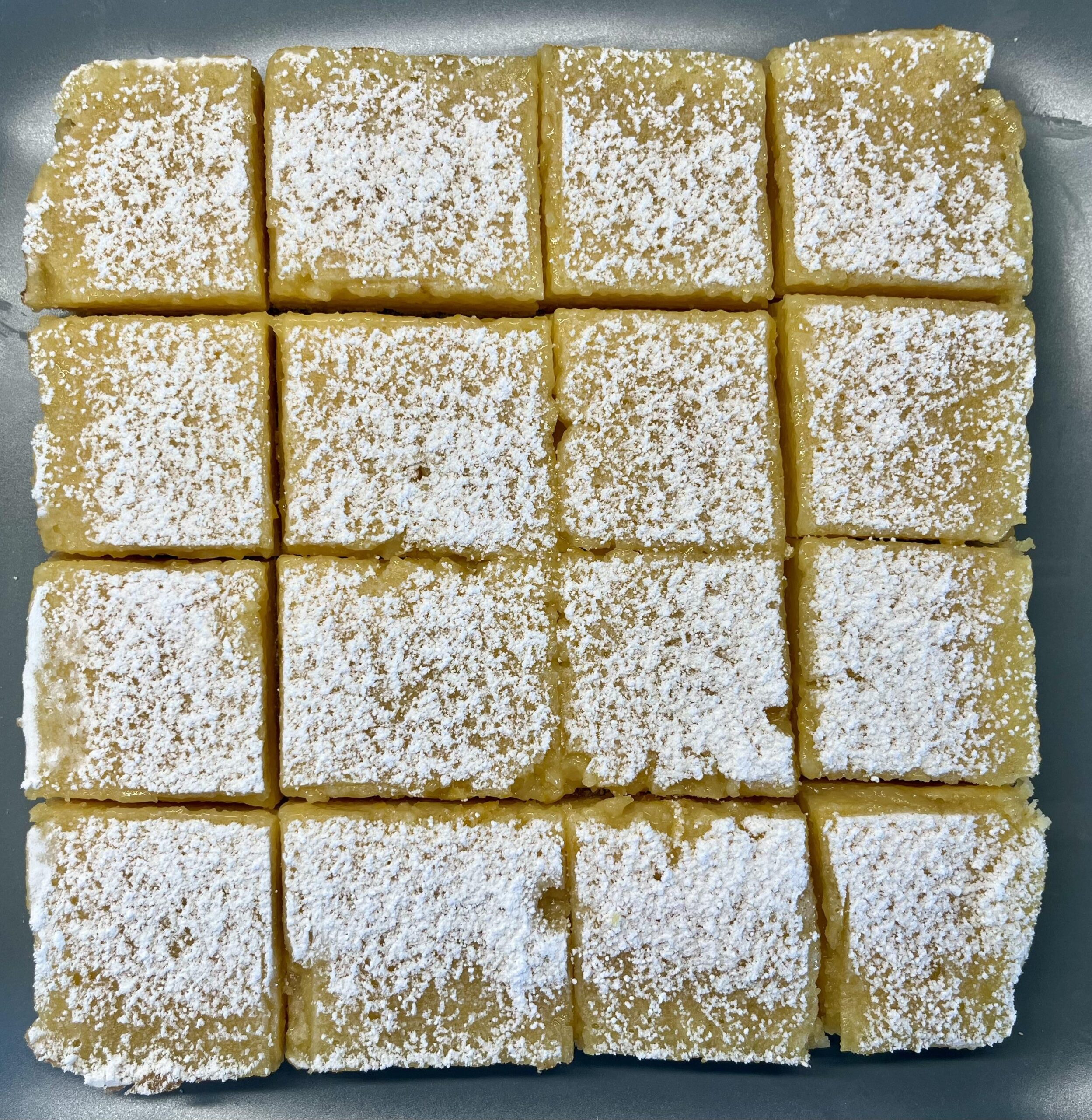 Soft yellow three-ingredient lemon bars dusted with powdered sugar in a white baking dish, with a fork lifting one square