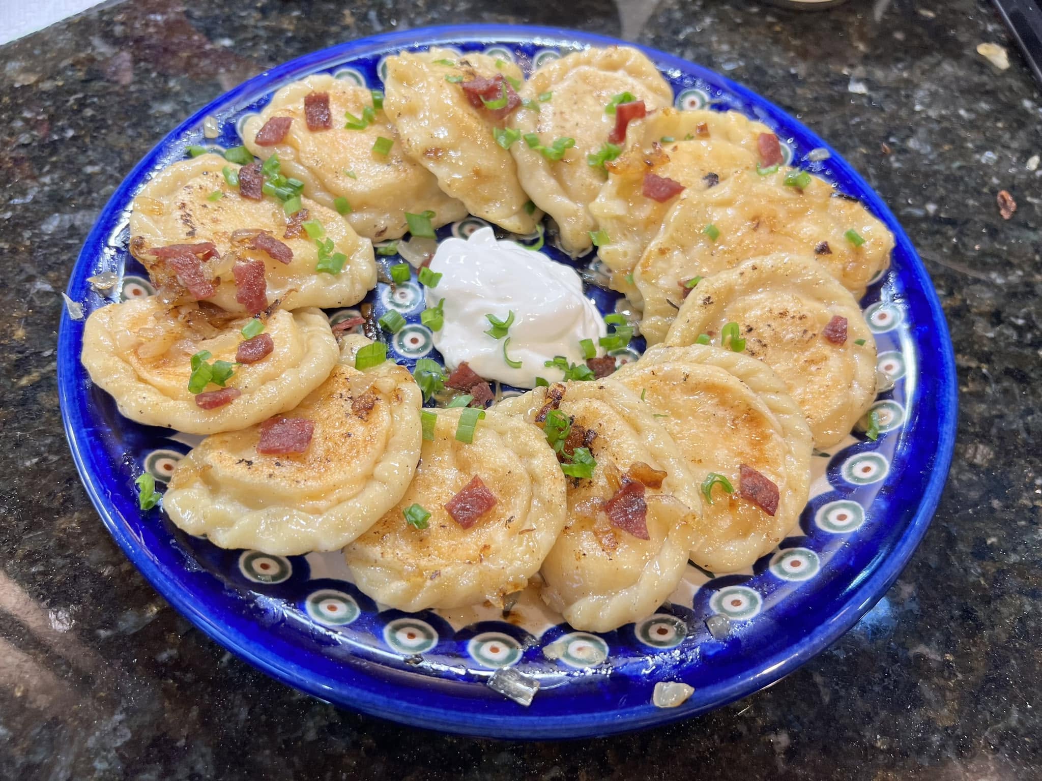 Homemade Polish pierogi with potato and cheese filling, topped with crispy bacon and chives.
