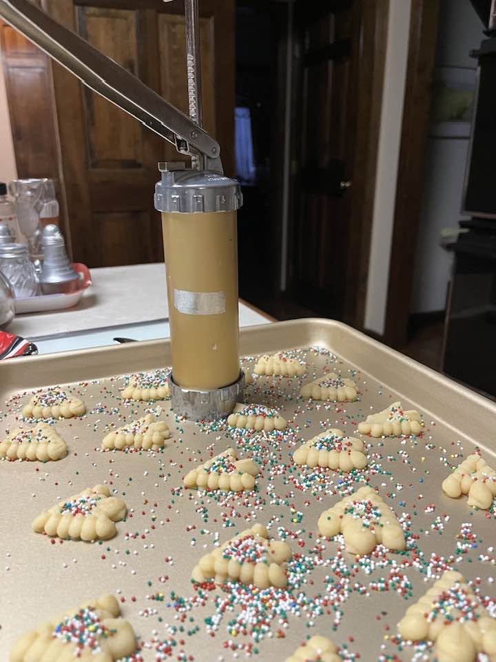 Old-fashioned spritz butter cookies shaped like Christmas trees, wreaths, and stars with festive red and green sugar on a vintage holiday cookie tray.