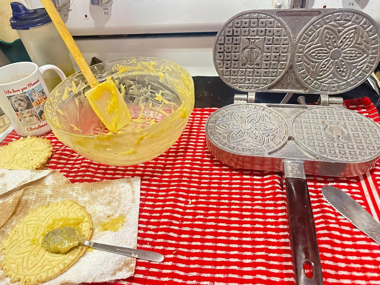 Homemade pizzelle cookie batter beside an open electric pizzelle iron ready for cooking.