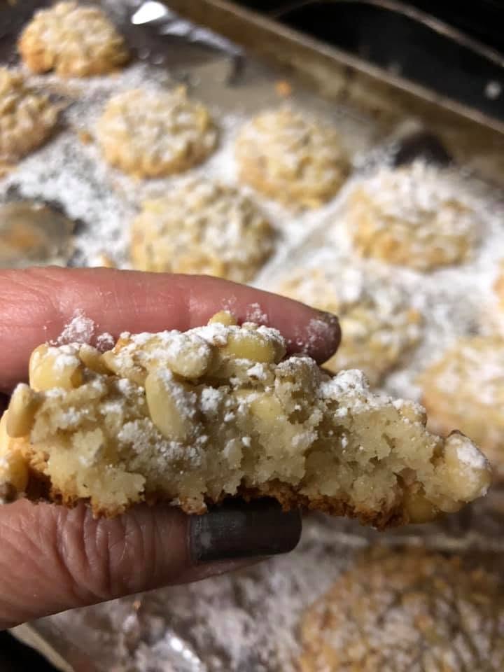 the close-up of a finished pignoli cookie held between the fingers, showing its soft almond center